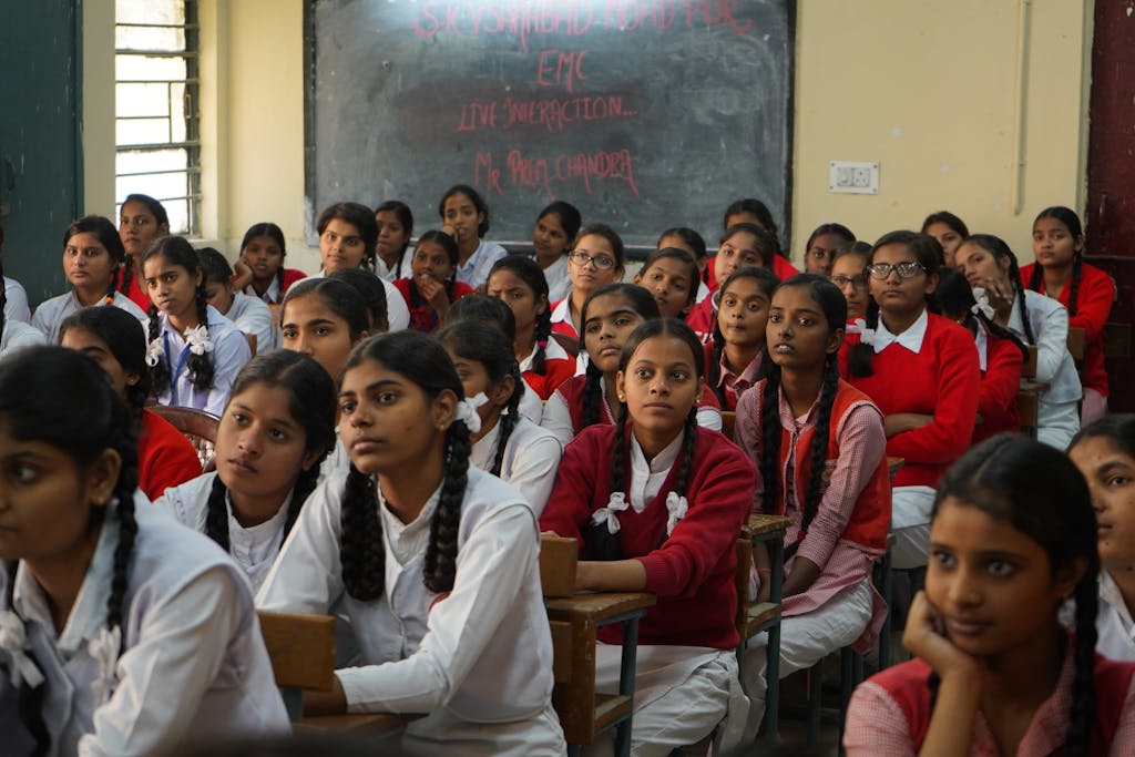 Group of Indian schoolgirls in uniform attentively listening in a classroom setting.